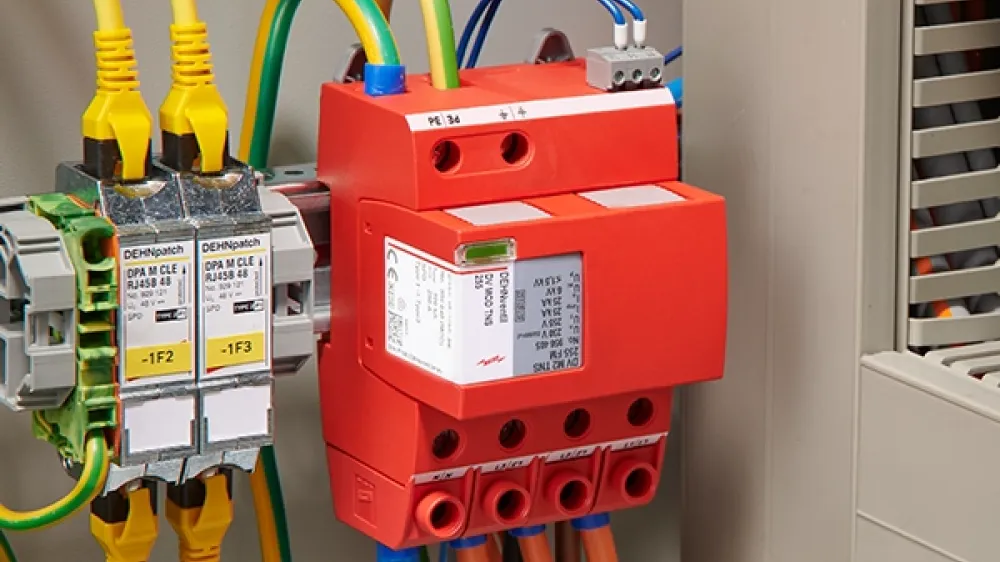 Red surge arrester, mounted and cabled next to an open switchgear cabinet.
