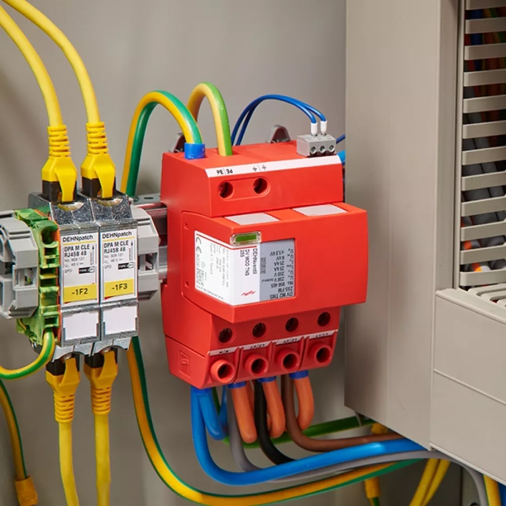 Red surge arrester, mounted and cabled next to an open switchgear cabinet.