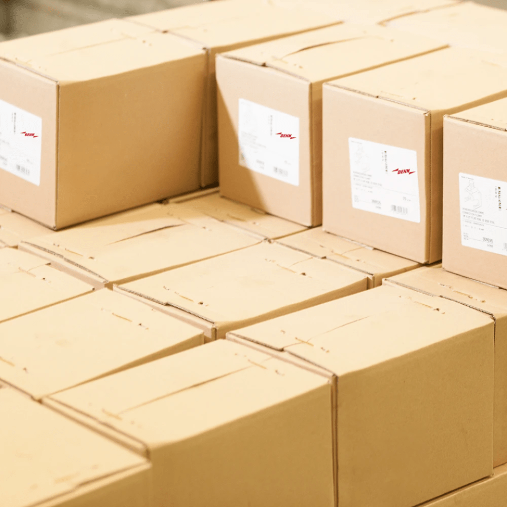 Stacked shipping boxes with DEHN product labels in a warehouse or dispatch area.