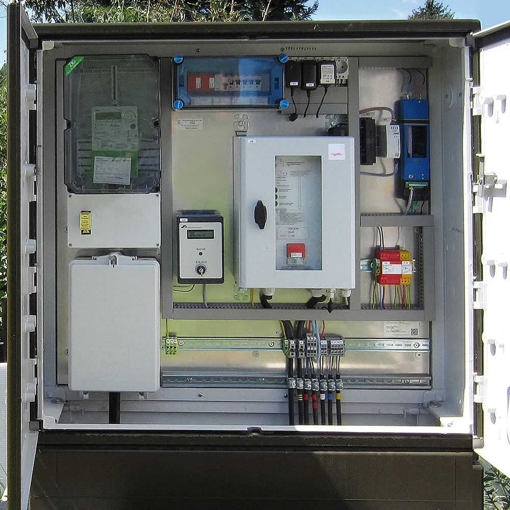 Open outdoor electrical cabinet showing meters, control units, wiring terminals, and surge protection components mounted on a panel.