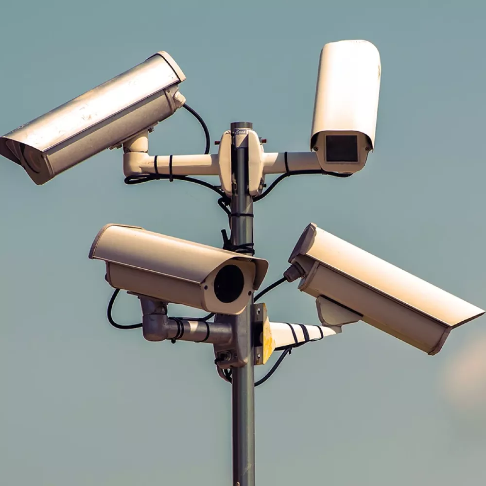 Outdoor surveillance pole with multiple security cameras mounted in different directions against a clear sky.