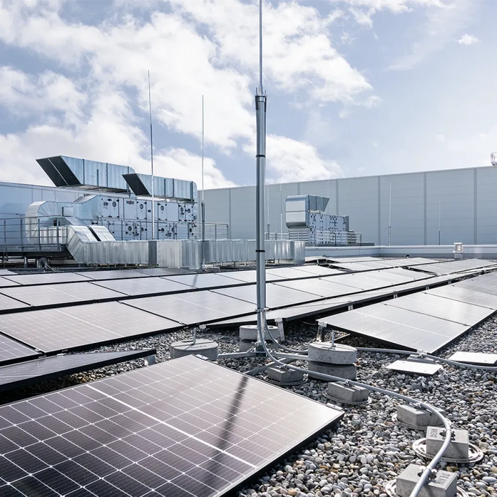 Rooftop photovoltaic system with solar panels, lightning protection mast, and cable routing on a commercial building roof under a cloudy sky.