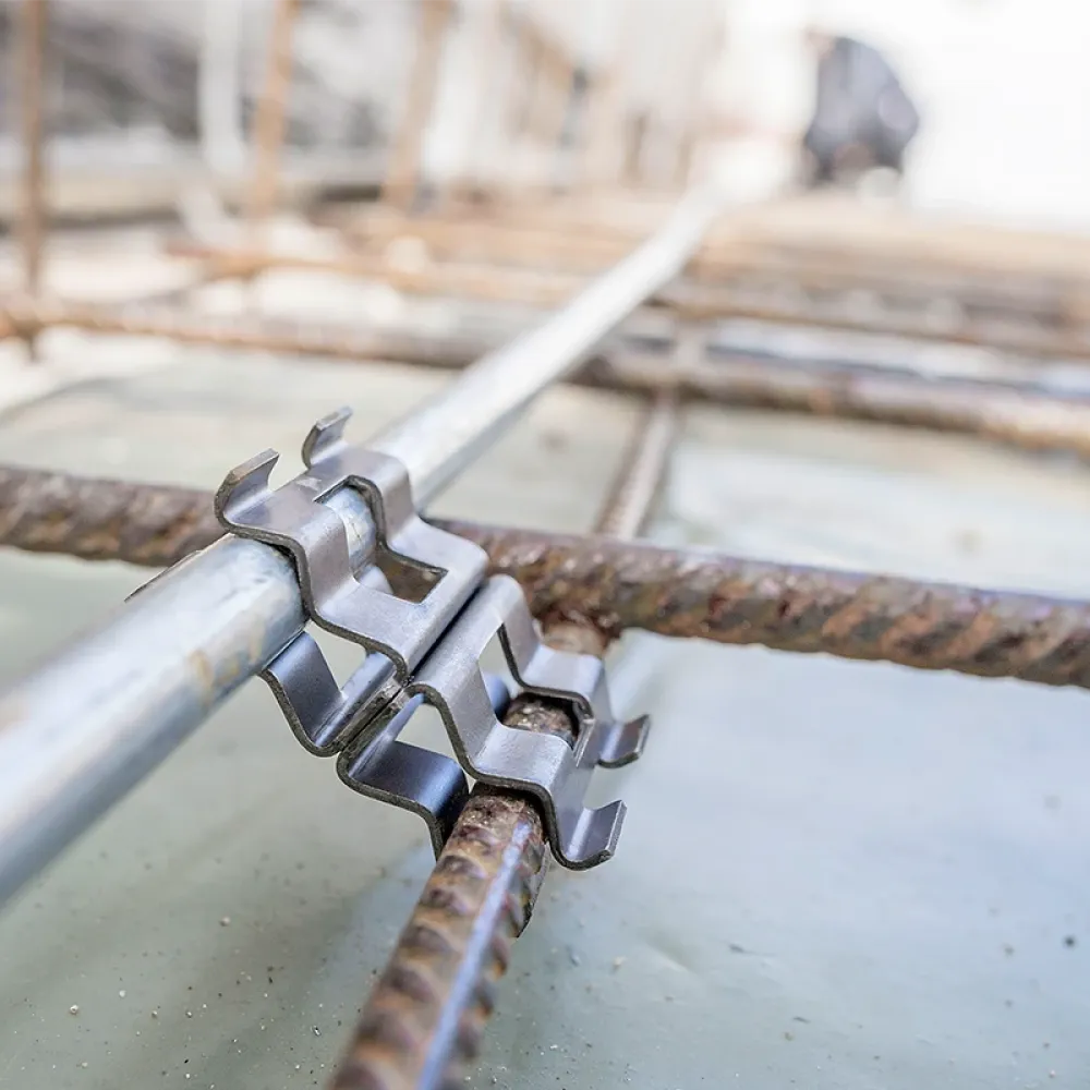 Close-up of a metal grounding clamp connecting a steel conductor to reinforcing rebar embedded in a concrete foundation slab.