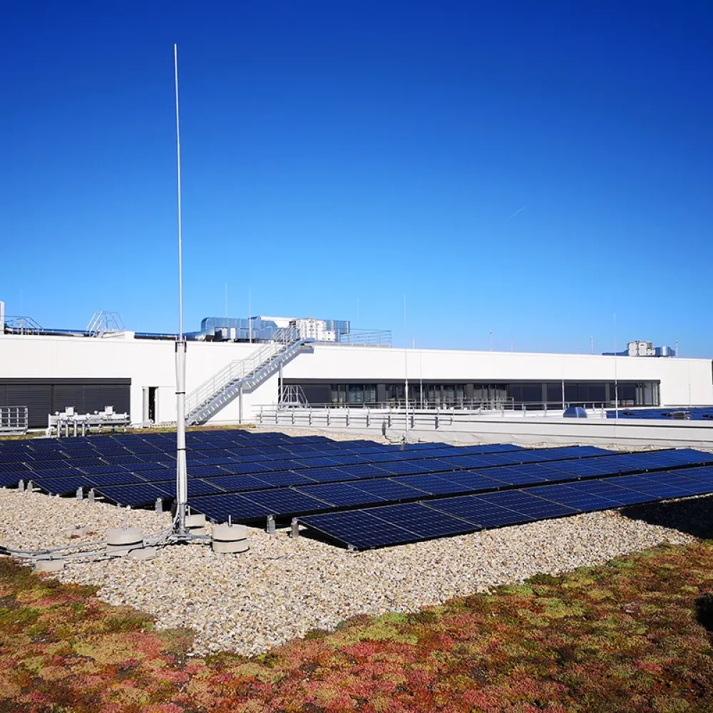 Rooftop solar panels installed on industrial building with lightning protection masts under clear blue sky.