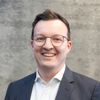 Portrait von Simon Thaler vor einem grauem Hintergrund.