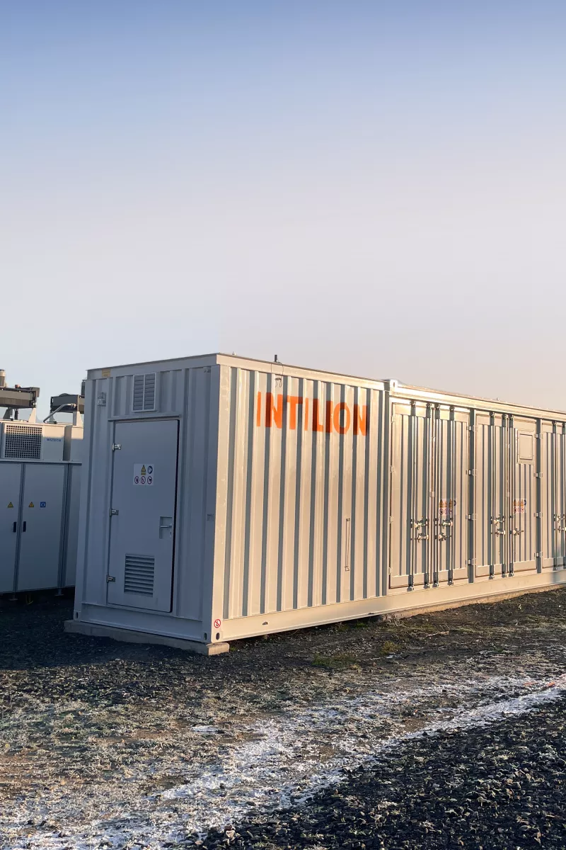 Große, hellgraue, modulare Container-Energieanlagen mit der Aufschrift INTILION inmitten von Solarzellen.