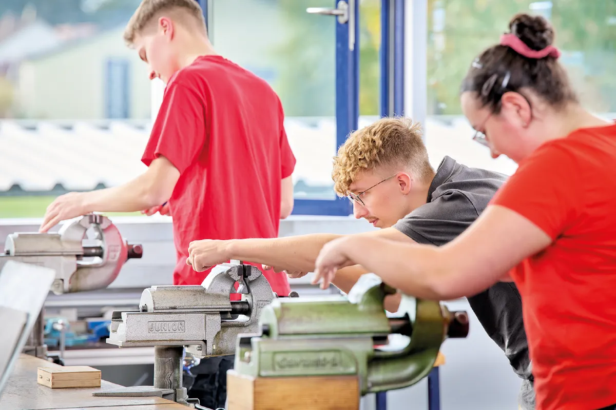 Three people working with metalworking machines in a workshop.