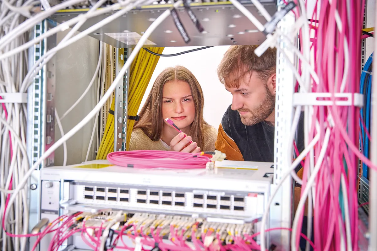 Two people working with network cables and equipment in a server rack.
